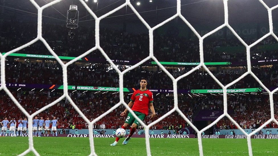 Hakimi takes the penalty kick, viewed through the goal netting