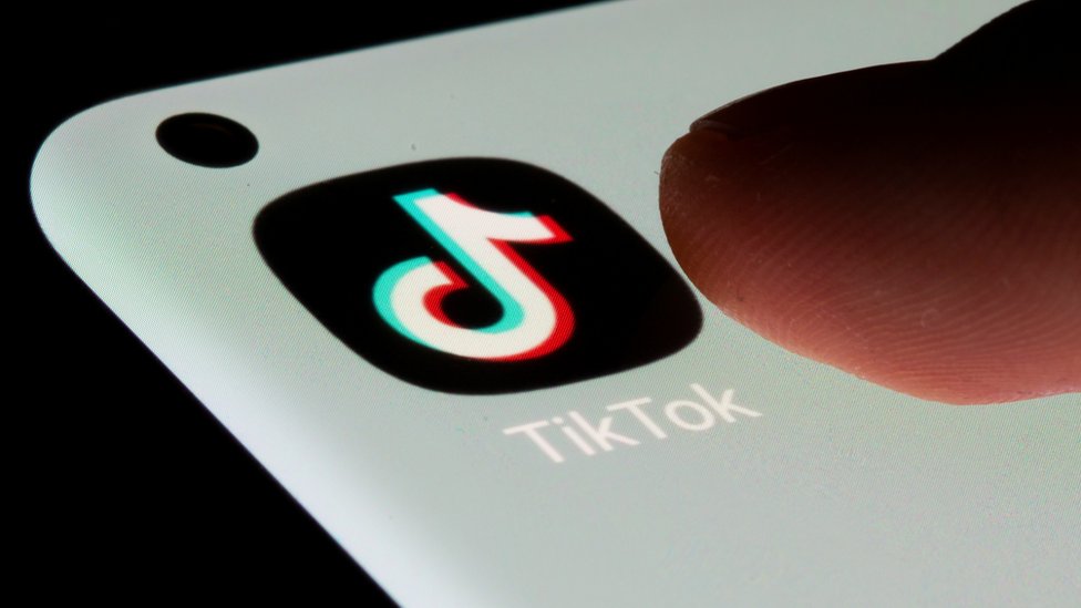 Thumb about to press TikTok app logo on a mobile phone screen.
