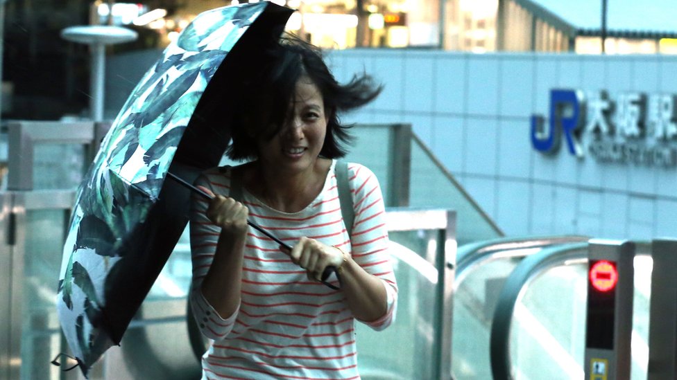 Žena se brani kišobranom od jakog vetra