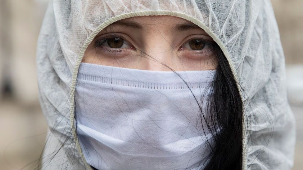 Una mujer joven vistiendo equipo de protección personal y mascarilla.
