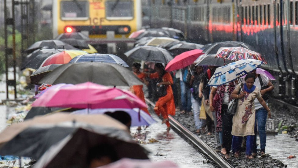 Люди идут по железнодорожным путям, когда сильные муссонные дожди обрушились на пригородные поезда возле Сиона 1 июля 2019 года в Мумбаи, Индия.