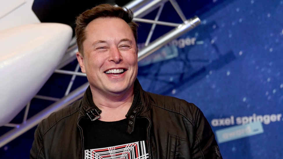 Elon Musk con una foto de un cohete espacial detrás,