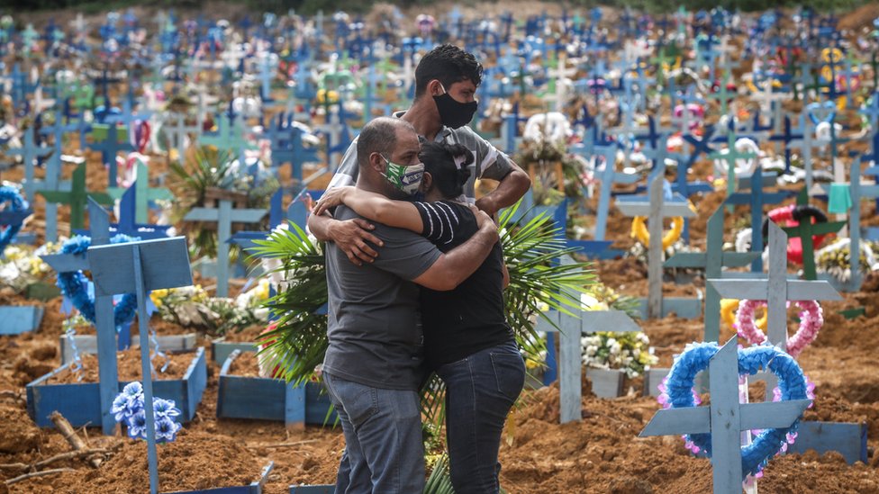 Родственники умершего в защитных масках скорбят во время массового захоронения коронавируса в Манаусе