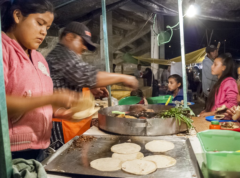 Señor preparando un taco en un mercado callejero iluminado apenas por una bombilla. Señor preparando un taco en un mercado callejero iluminado apenas por una bombilla.