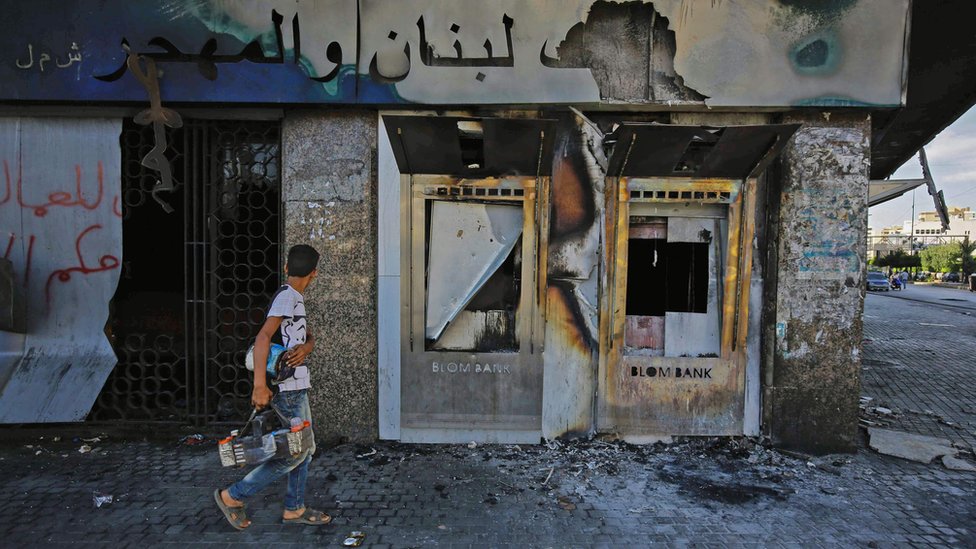 A youth walks past a burnt-down branch of a Lebanese bank in al-Nour Square in Tripoli, Lebanon (12 June 2020)