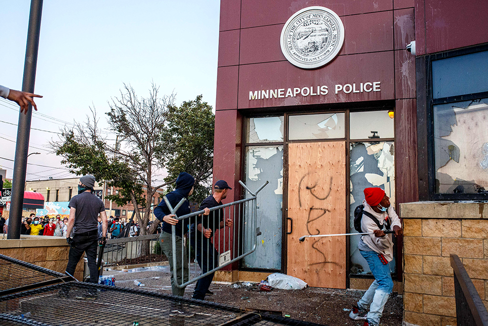 Protesters use a barricade to try and break the windows of the 3rd Police Precinct