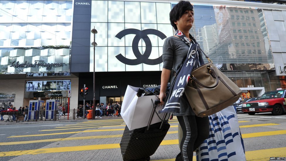 Турист из материкового Китая пересекает улицу с множеством сумок с покупками в районе Цим Ша Цуй в Гонконге.