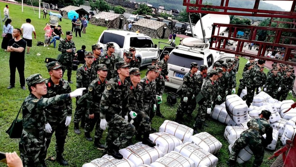 Военизированная полиция выгружает пакеты помощи при стихийных бедствиях из грузовика во временном поселении после землетрясения в округе Чаннин, провинция Сычуань, Китай, 18 июня 2019 г.