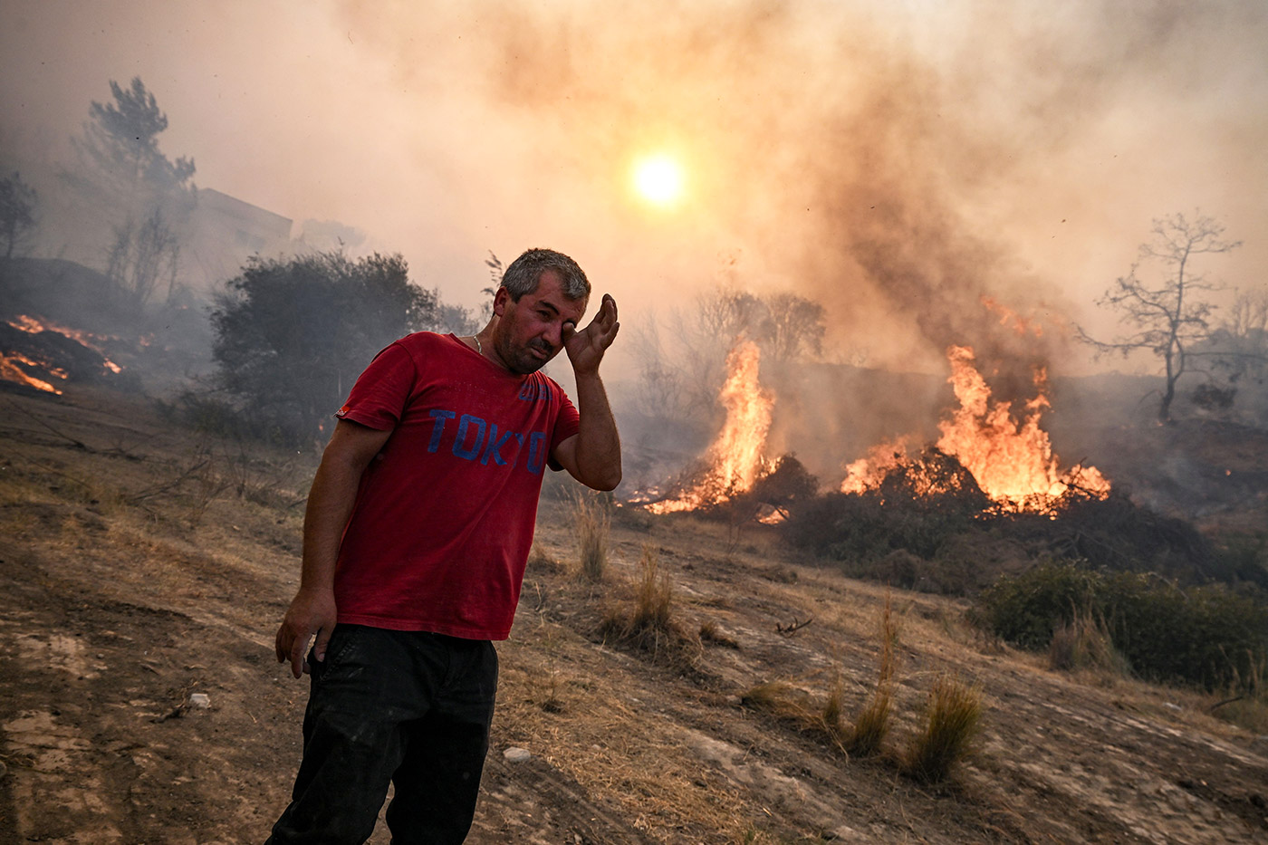 A man rubs his eyes as a fire burns into the village of Gennadi on the Greek Aegean island of Rhodes - 25 July 2023