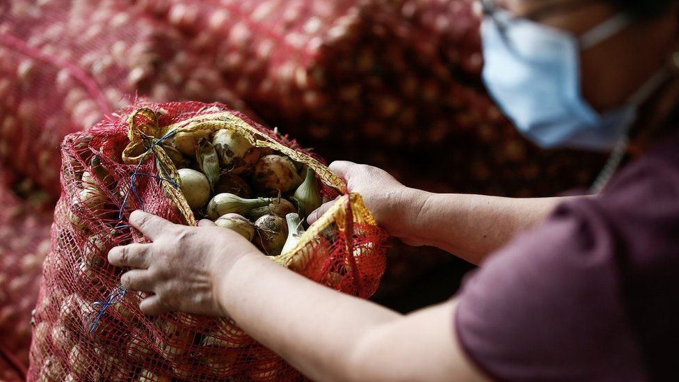Una mujer abre una bolsa llena de cebollas