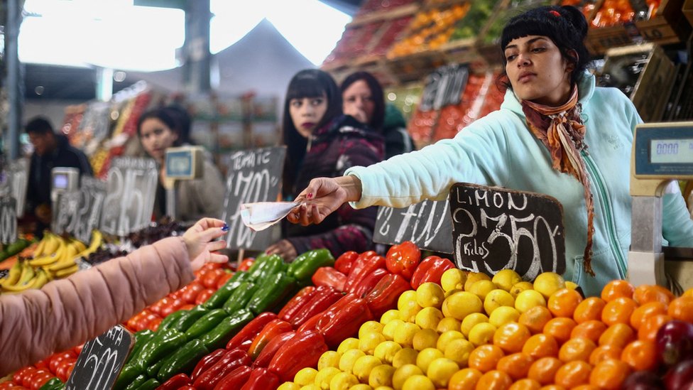 A saleswoman gives change to a customer at a greengrocer's shop in Buenos Aires