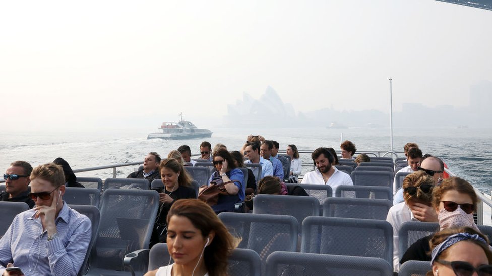 Пассажиры на пароме в гавани Сиднея в дыму над городом, который почти закрыл Сиднейский оперный театр на заднем плане