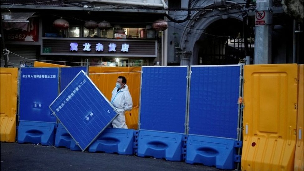 FILE PHOTO: A worker in a protective suit keeps watch next to barricades set around a sealed-off area, during a lockdown to curb the spread of the coronavirus disease (COVID-19) in Shanghai, China April 11, 2022
