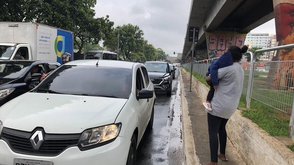 Caroline Silveira e sua filha mais nova, no colo, em meio a carros