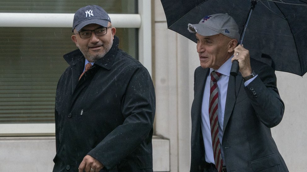 Abogados de El Chapo caminando hacia la corte bajo una sombrilla.