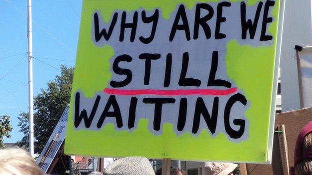 Вывеска протестующего с надписью «Почему мы все еще ждем?»