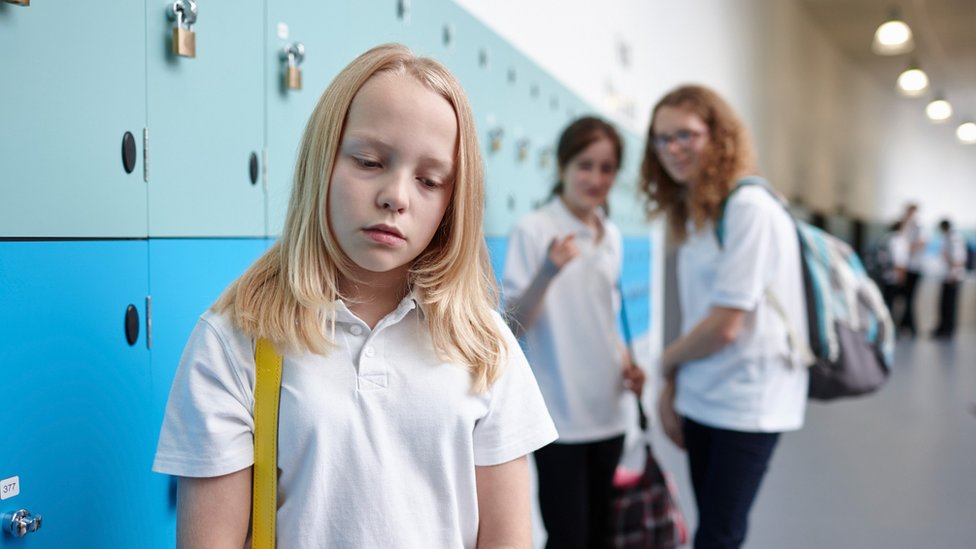 Two girls look at a girl who looks upset by what they are saying