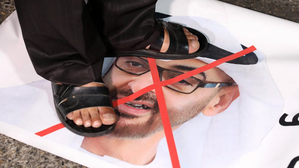 Палестинский демонстрант стоит на фотографии наследного принца Абу-Даби Мухаммеда бен Заида на протесте в Вифлееме против решения ОАЭ нормализовать отношения с Израилем (16 августа 2020 г.)