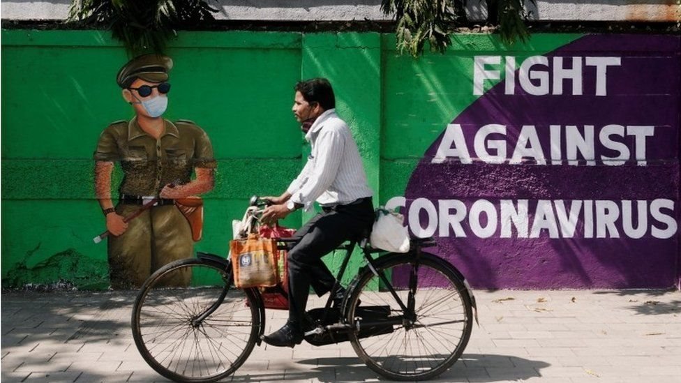 Warga India bersepeda di depan mural virus corona