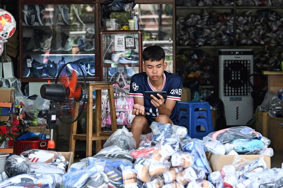 一名年輕人在河內一家體育用品店等待顧客時玩手機（2023年6月20日）。