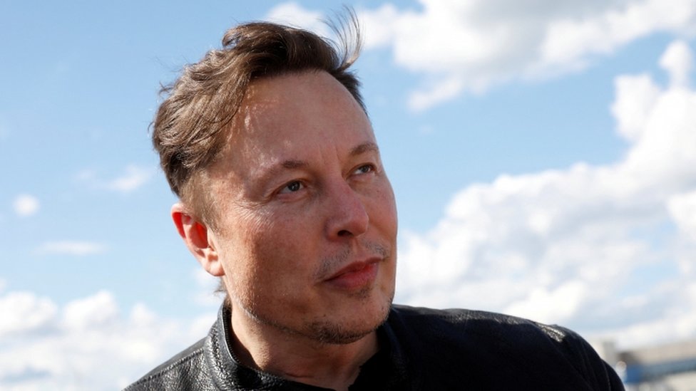 Elon Musk olhando para o lado, sob céu azul