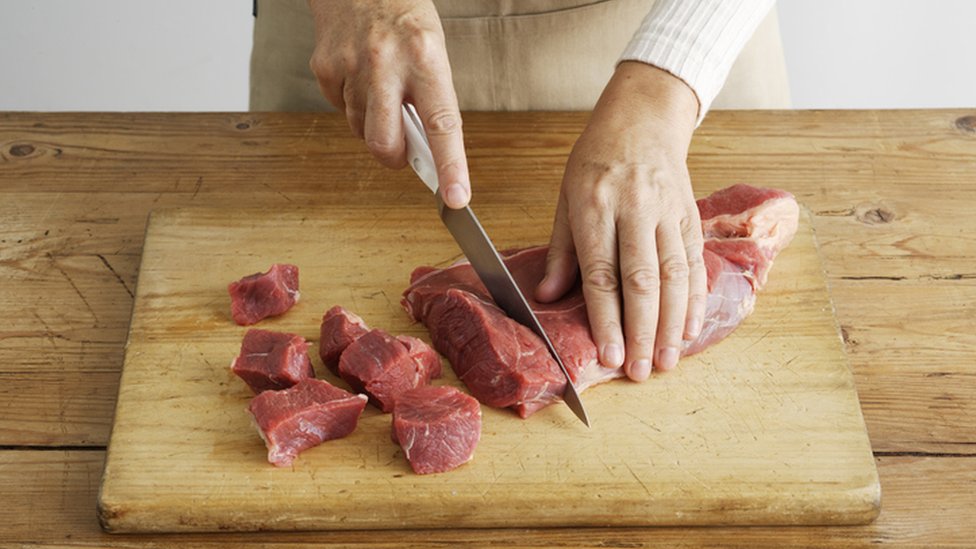 Una persona corta carne de res sobre una tabla de madera