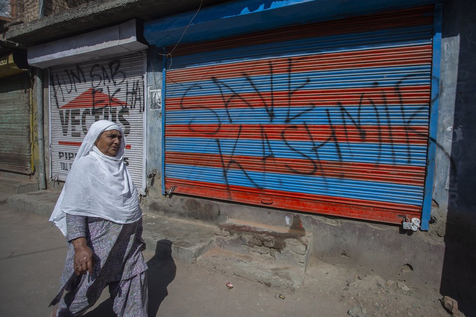A woman walks past a wall with graffiti on it, which reads: "Save Kashmir"