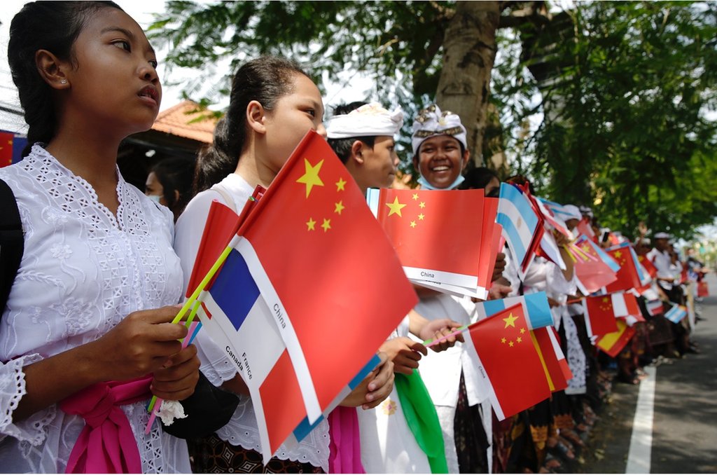 巴厘島學生在國際機場附近的一條街道上，揮舞著G20成員國的旗幟，歡迎出席峰會的領導人抵達巴厘島。