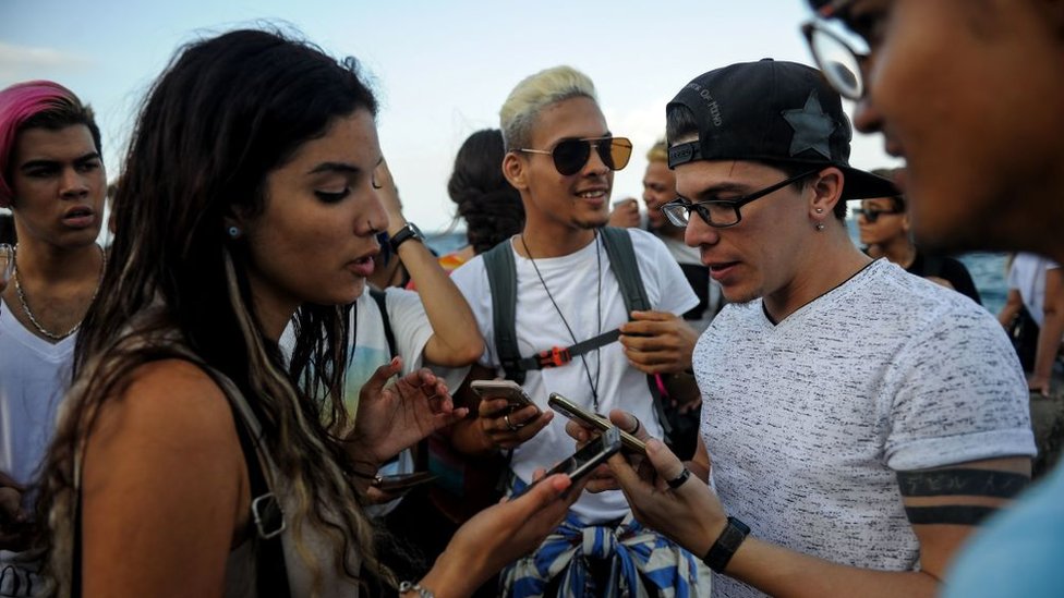 Jóvenes miran sus teléfonos en el Malecón de La Habana.