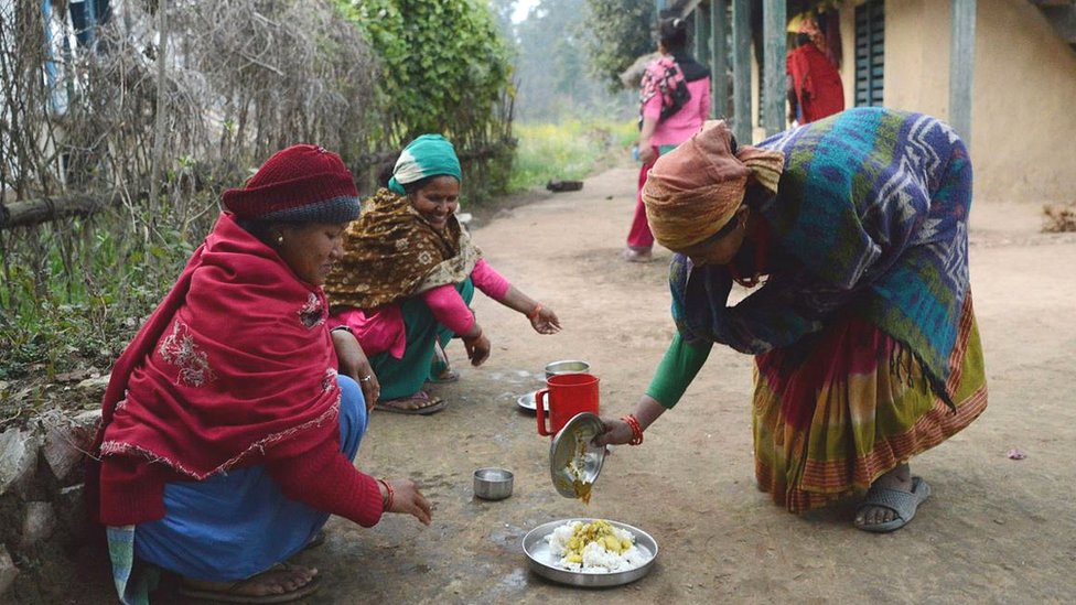 A Nepali woman being served food outside her home