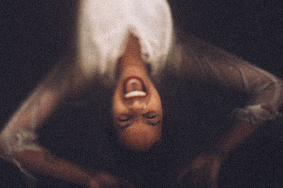 A woman in a white dress screaming while laying back in dark water