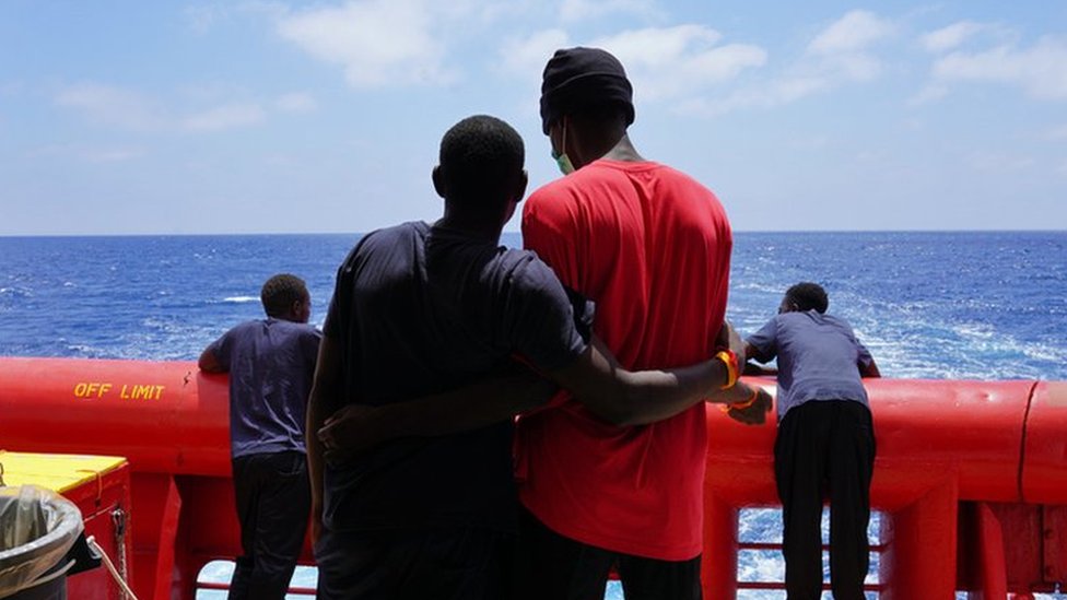 The backs of two men looking out to sea from the deck of the SOS Mediterranee