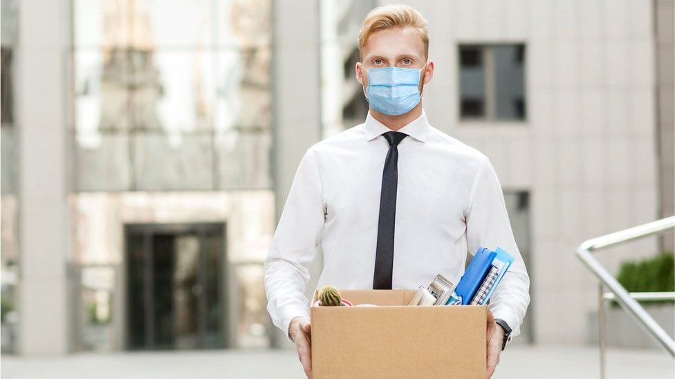 Стоковое изображение человека в маске, несущего коробку со своими вещами из офиса