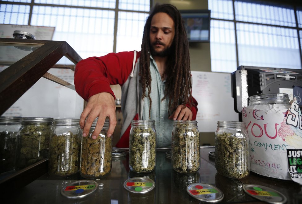 Волонтер Чарли Кирчхаймер демонстрирует банки с сушеными бутонами каннабиса в коллективном диспансере медицинской марихуаны Ла Бреа в Лос-Анджелесе