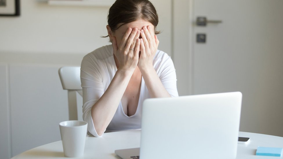 Woman with her face in her hands in front of laptop