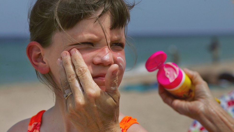 Mujer aplicando crema solar a una niña.