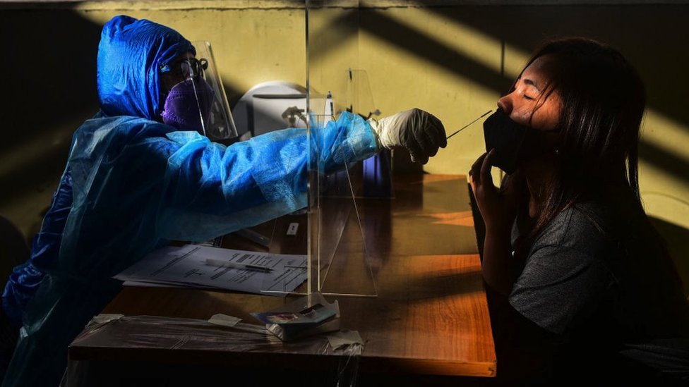 Profissional de saúde fazendo teste de covid em uma mulher em Manila