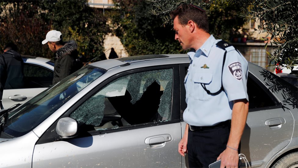 Израильский полицейский смотрит на машину, поврежденную в результате обстрела в Старом городе Иерусалима