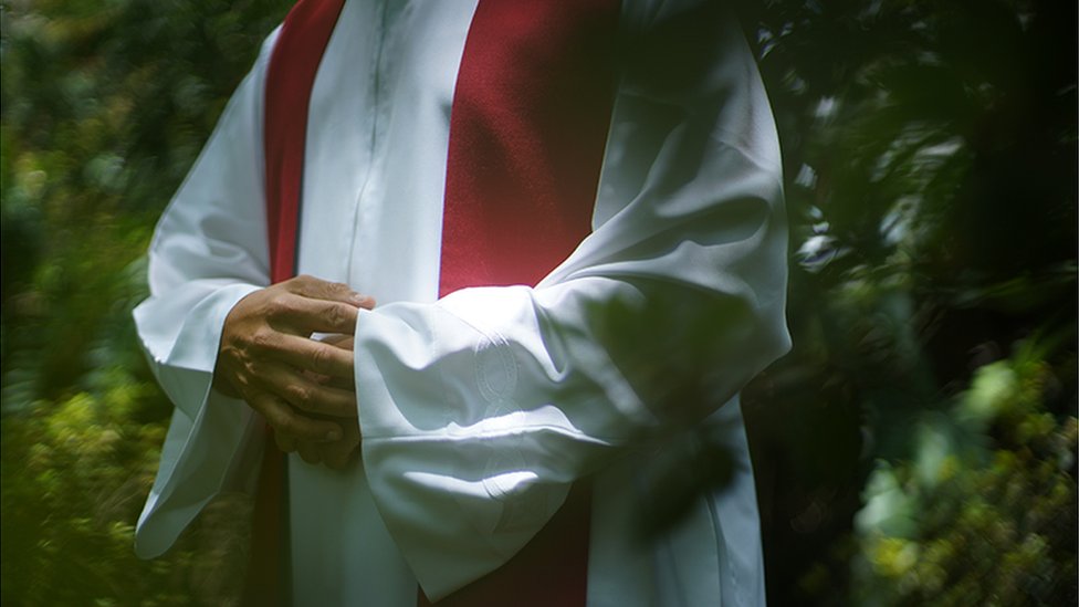 Un sacerdote con alba blanca y una estola bermellón sobre los hombros