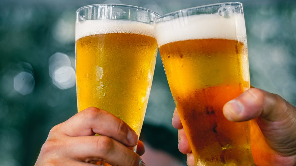 Mãos seguram dois copos de cerveja gelada