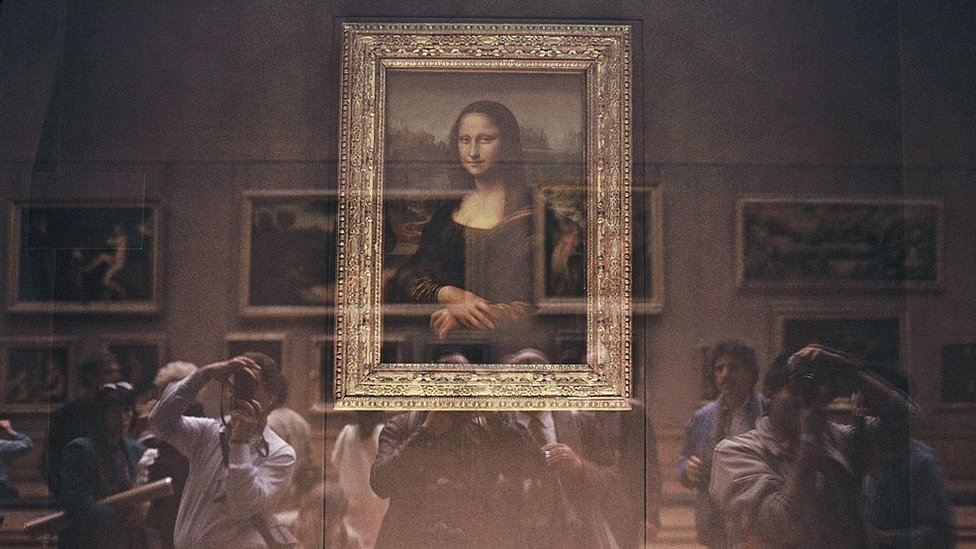 La Mona Lisa detrás de su protección de vidrio a prueba de balas con turistas japoneses en el Museo del Louvre.
