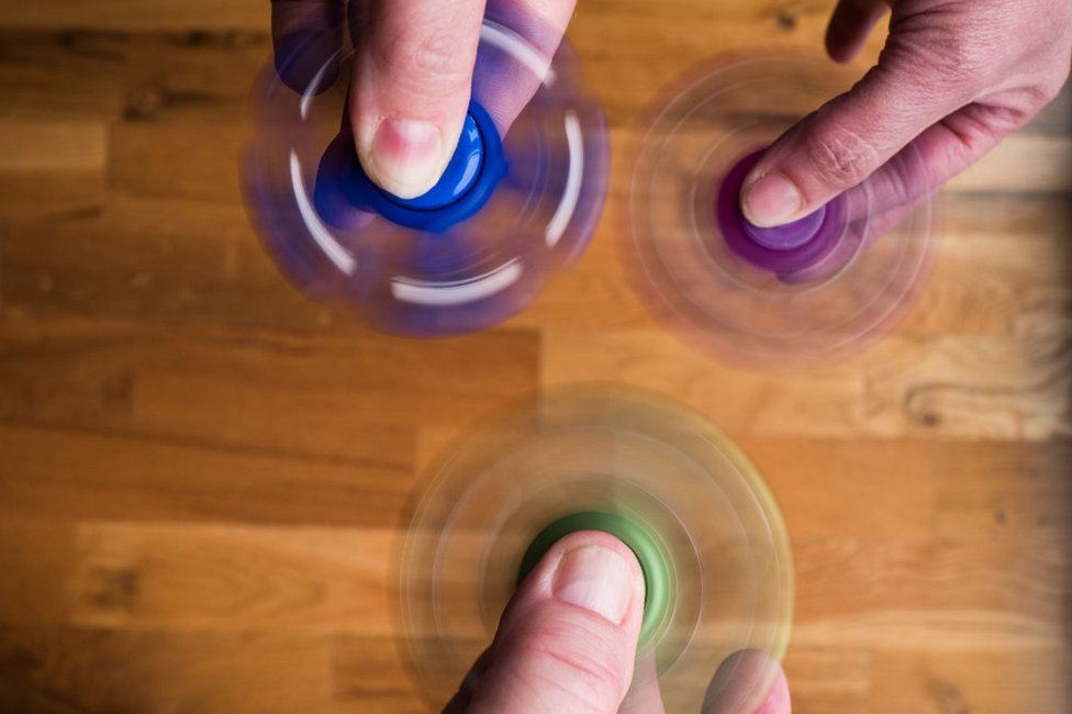Los fidget spinner están dejando de ser un juego de niños... Tres personas hacen girar sus fidget spinners