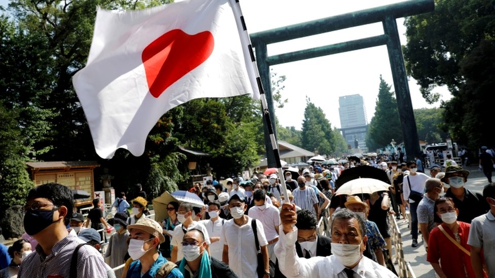 People walk through a Torii gate with a Japanese national flag as they visit Yasukuni Shrine