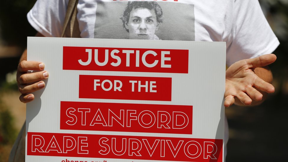 Женщина держит табличку с надписью «Справедливость для пережившей Стэнфордское изнасилование»