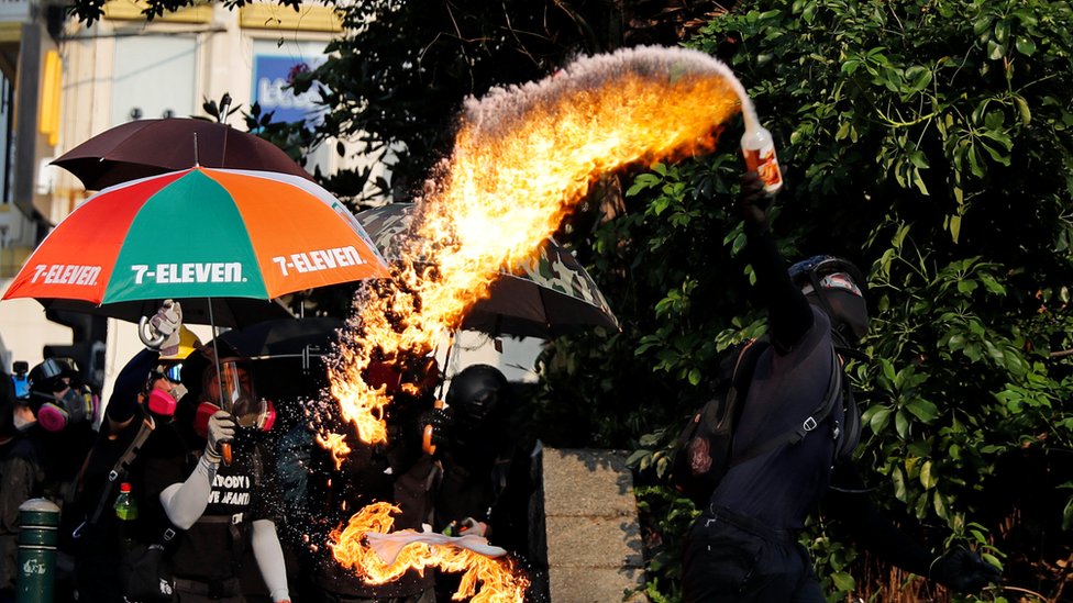 Дуга огня вырывается из бензиновой бомбы в бутылке, когда одетый в черное протестующий бросает ее