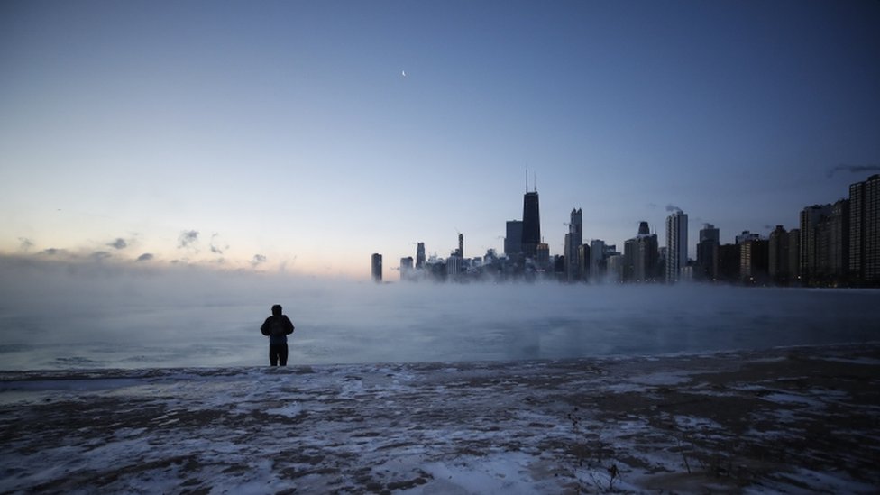 A man walks on North Avenue Beach as the sun rises over Lake Michigan in Chicago, Illinois