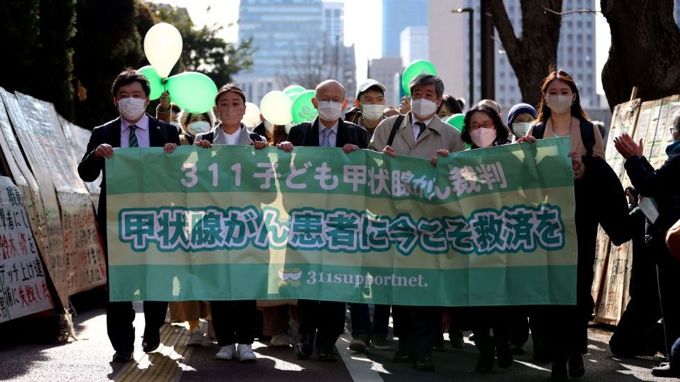 Masked supporters and lawyers of the six young plaintiffs hold a banner outside the Tokyo court
