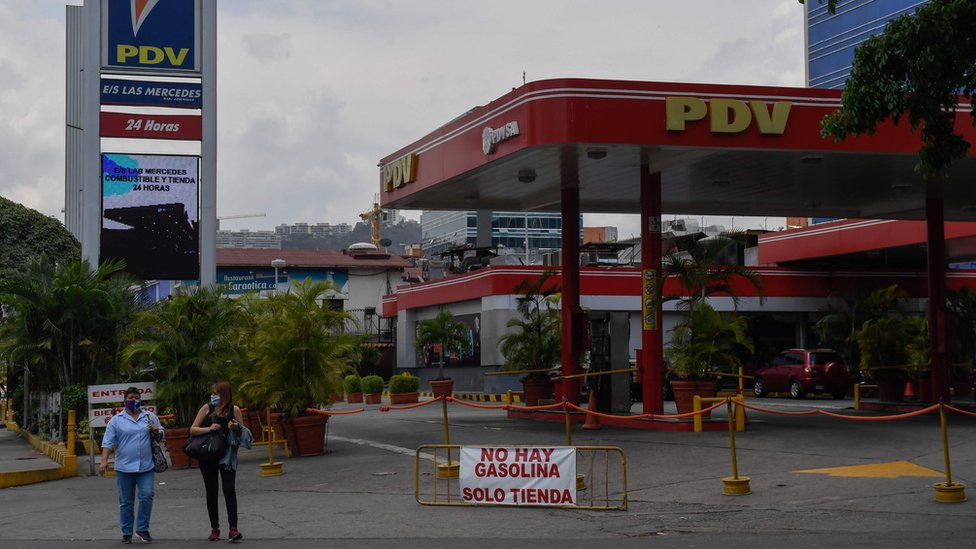 Люди проходят мимо закрытой автозаправочной станции в Каракасе, Венесуэла (14 мая 2020 г.)