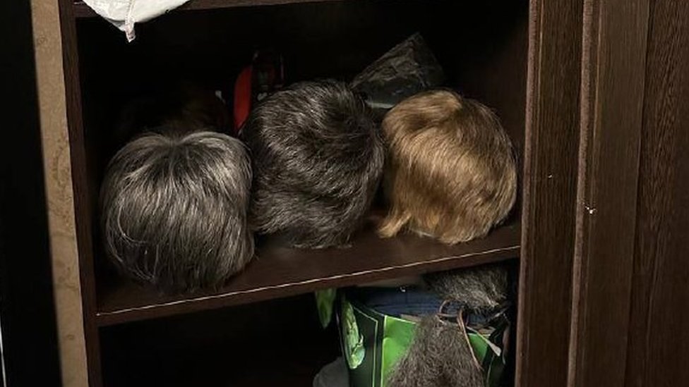A cupboard with several wigs inside