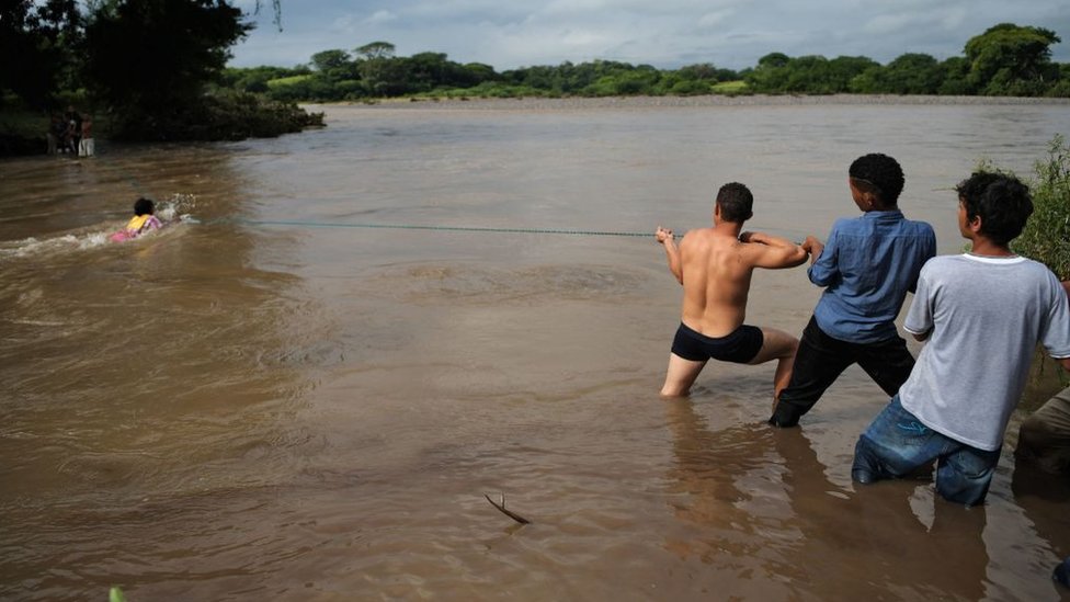 Jóvenes sujetan una cuerda para facilitar el paso por el río Goascorán.